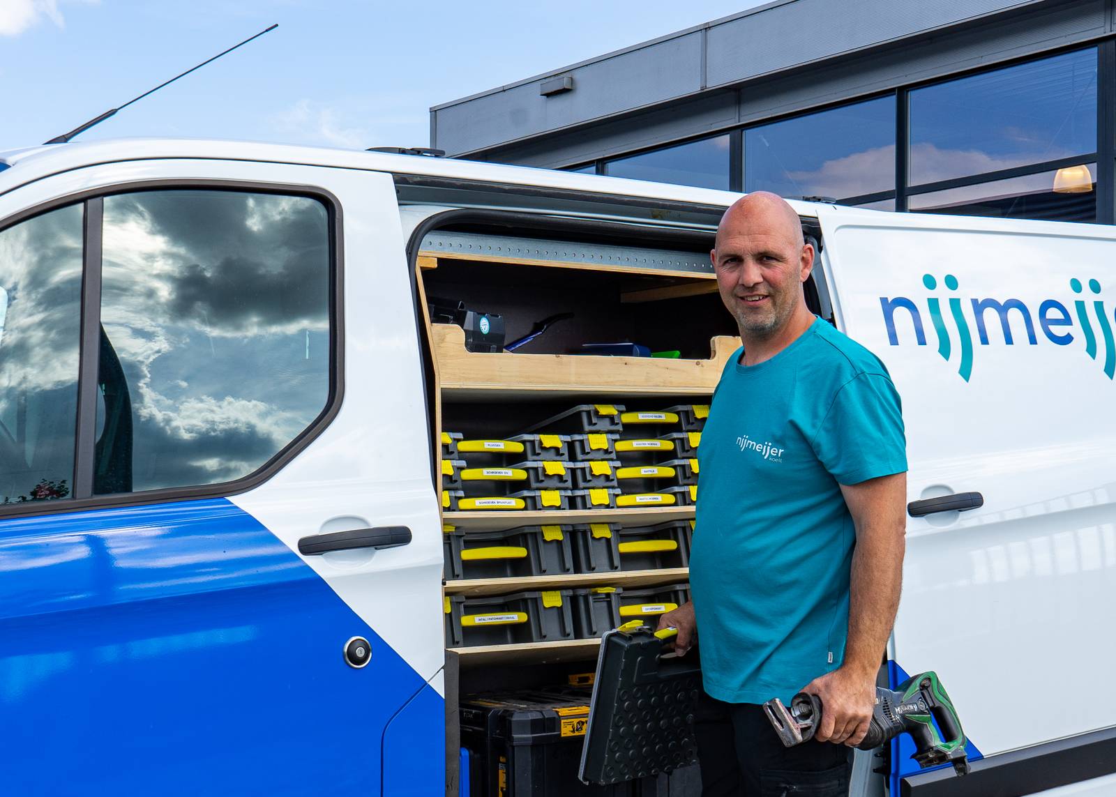 Medewerker van Nijmeijer Koelt staat voor een werkbus met open deur met gereedschap.