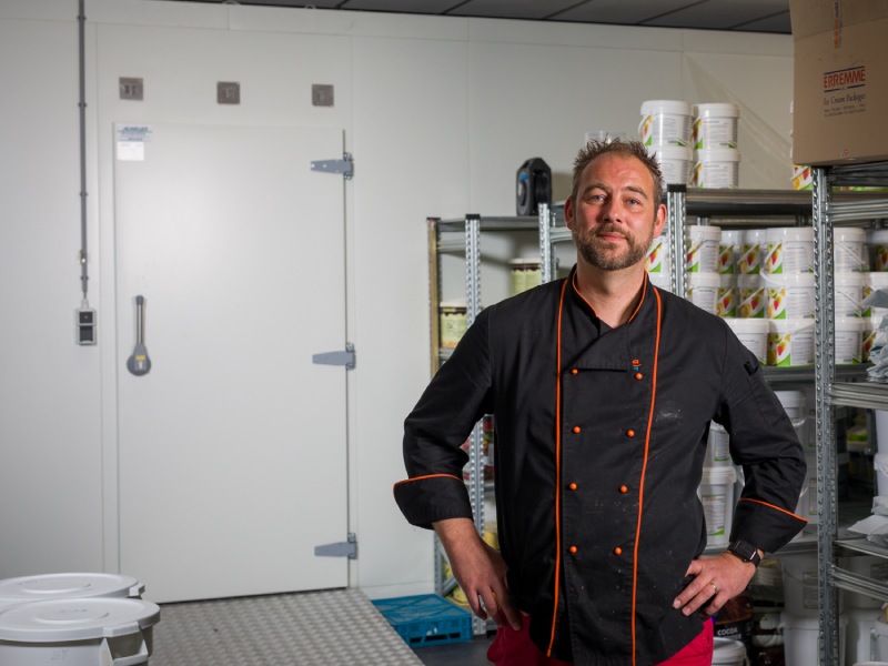 Man in bedrijfskleding staat trots geposeerd voor een grote vriescel.